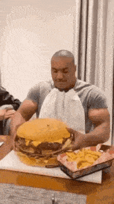 a man is sitting at a table eating a giant hamburger and french fries .