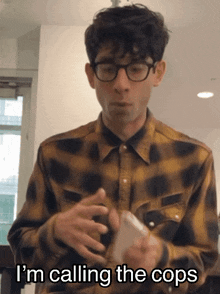 a man wearing glasses and a plaid shirt is holding a cell phone and saying i 'm calling the cops