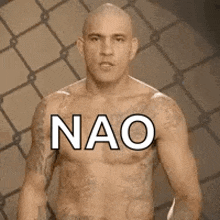 a bald man with tattoos on his chest is standing in front of a fence .