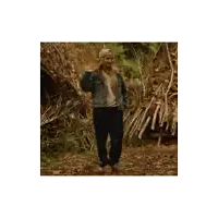 a woman in a denim jacket is standing in front of a pile of branches