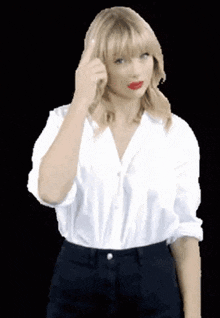 taylor swift is wearing a white shirt and black pants and giving a middle finger .
