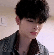 a close up of a young man wearing a denim jacket and a necklace with a cross .