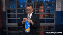 a man in a suit and tie holds a bag of potato chips