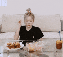 a woman wearing a black shirt with a fox embroidered on it is sitting at a table with a plate of food
