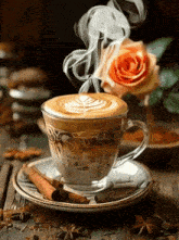 a cup of cappuccino with smoke coming out of it and a rose in the background