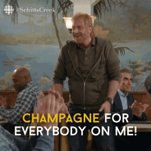a man stands in front of a group of people with champagne for everybody on me written below him