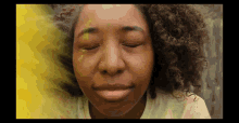 a close up of a woman 's face with her eyes closed and yellow paint coming out of her hair