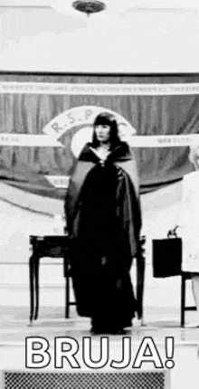 a black and white photo of a woman in a black dress standing in front of a stage .