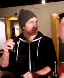 a man wearing a beanie holds a bottle of beer