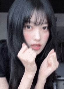 a young girl with long black hair is making a heart shape with her hands .