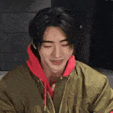a young man wearing a green jacket and a red hoodie smiles